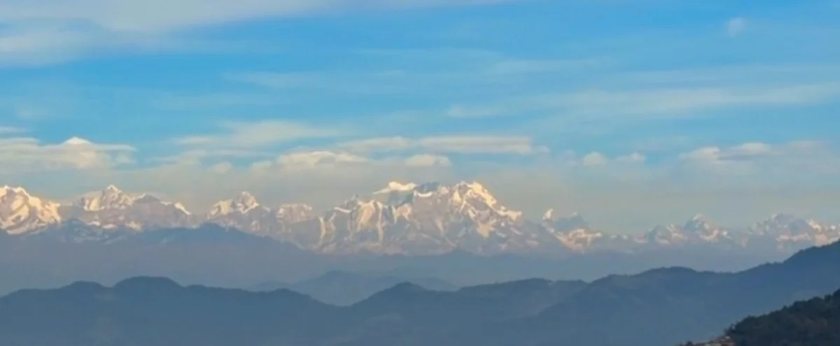 A long line of snow-capped Himalayan peaks above blue ridges on a clear morning near Mussoorie