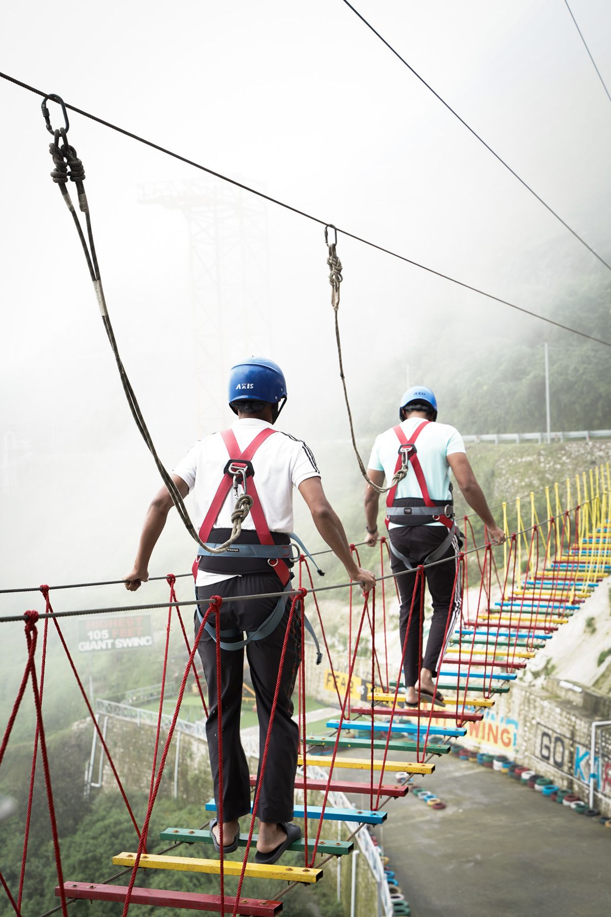 Two people in harnesses crossing the colourful Sky Bridge at High Fly Adventure, Mussoorie
